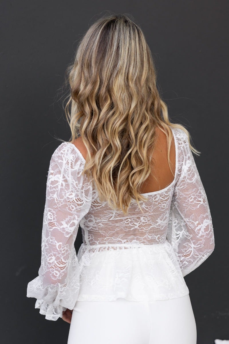 Back view of an elegant lace top with puffed sleeves and a peplum hem in white, worn by a model with wavy hair.