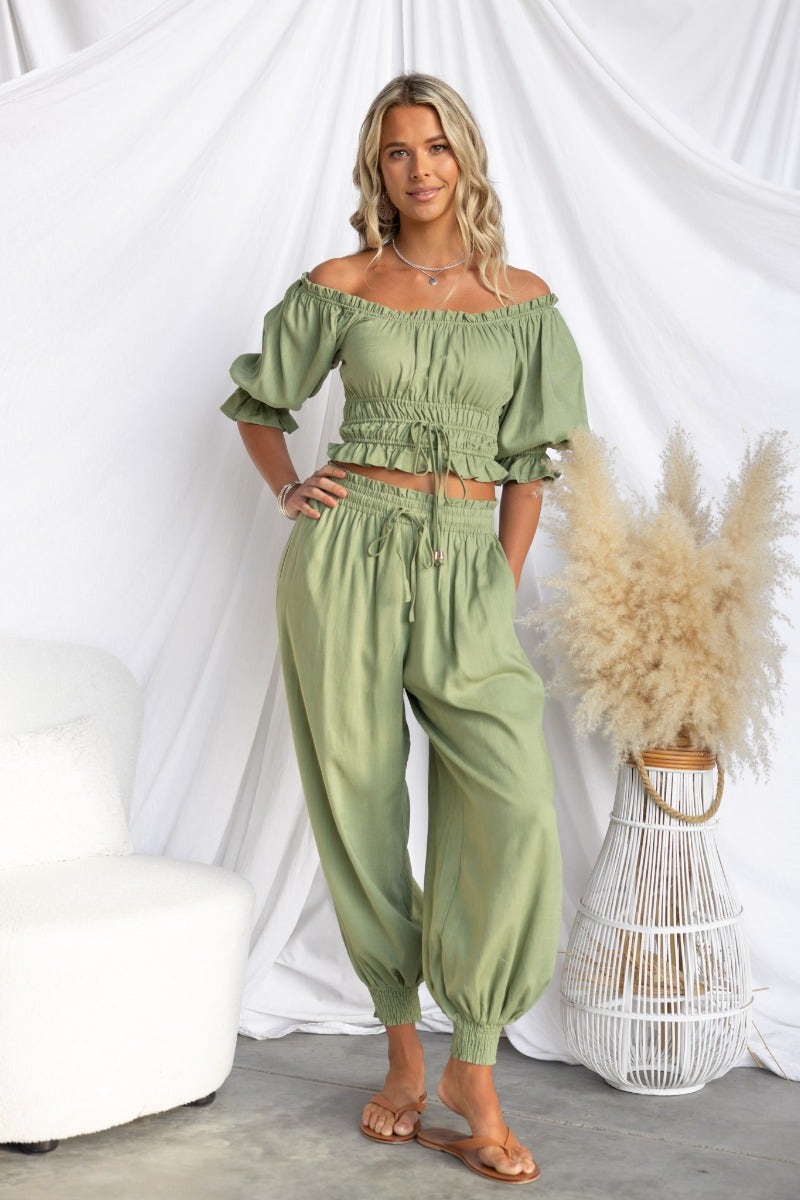 Model wearing Karma Pants with elastic waistband and drawstring, styled with an off-shoulder top, in a serene green color.