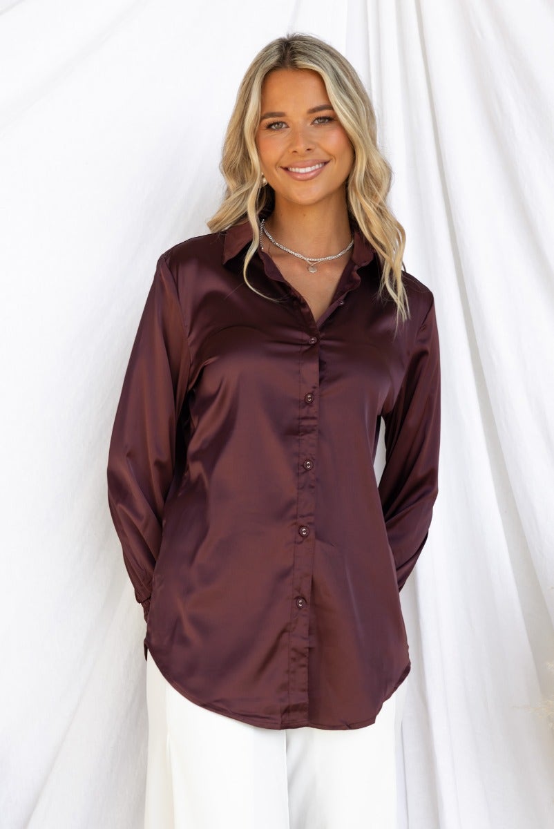Model wearing a Daina satin shirt in deep burgundy with button-up front and elastic cuffs, styled with relaxed fit.