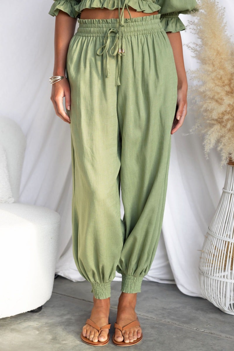 Karma pants in olive green with elastic waistband and cuffs, styled with a matching top and minimalist accessories.