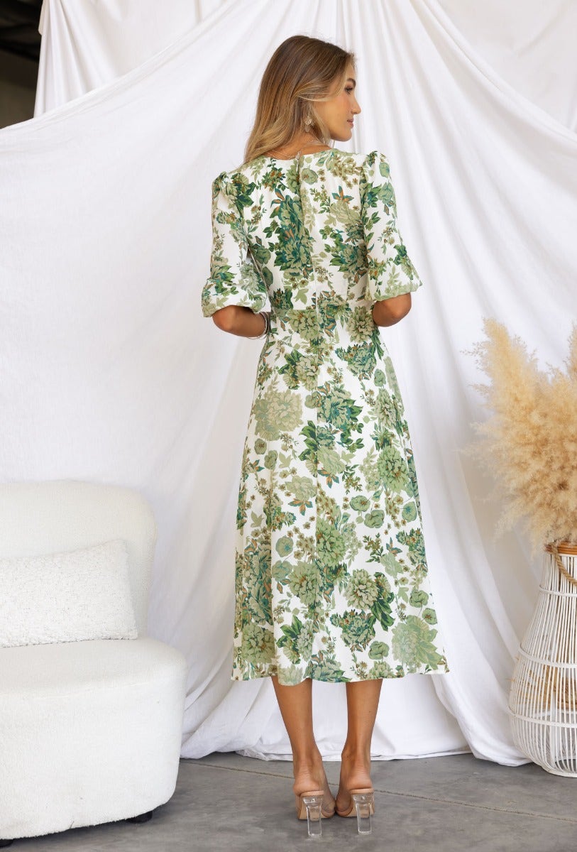 Back view of woman in floral print Corria midi dress with twist detail and elastic sleeve cuffs.