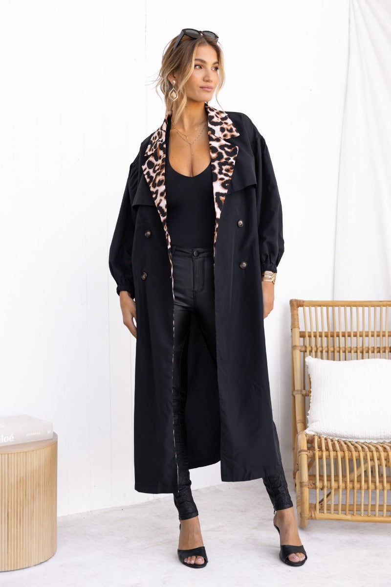 Stylish woman wearing the Oxley Coat, a black trench with leopard print detail and button-up front.