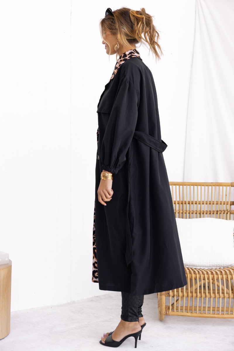 Side view of a black trench coat featuring animal print detail, removable tie, and elastic cuffs, ideal for stylish layering.