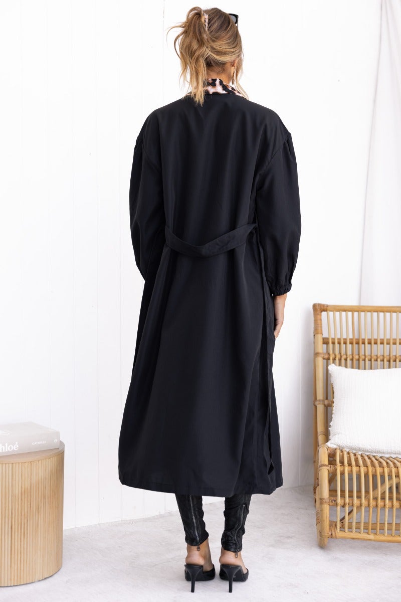 Back view of a lightweight black trench coat with a removable fabric tie and elastic cuffs, styled for a modern look.