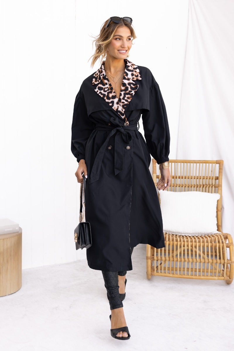 Chic woman wearing a black trench coat with animal print collar, featuring a button-up front and removable tie.