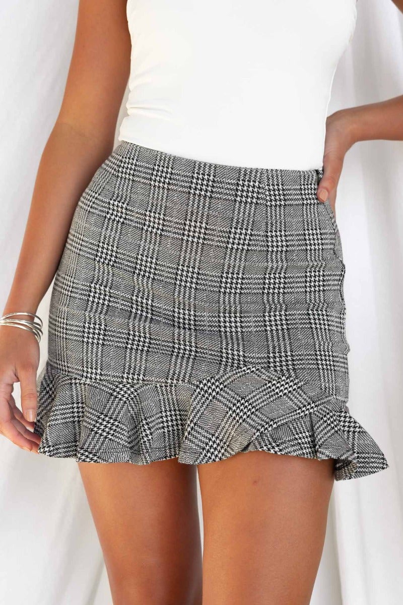 Thelma Houndstooth skirt with ruffle hem, featuring side invisible zip and stretchy material, styled with a fitted top.