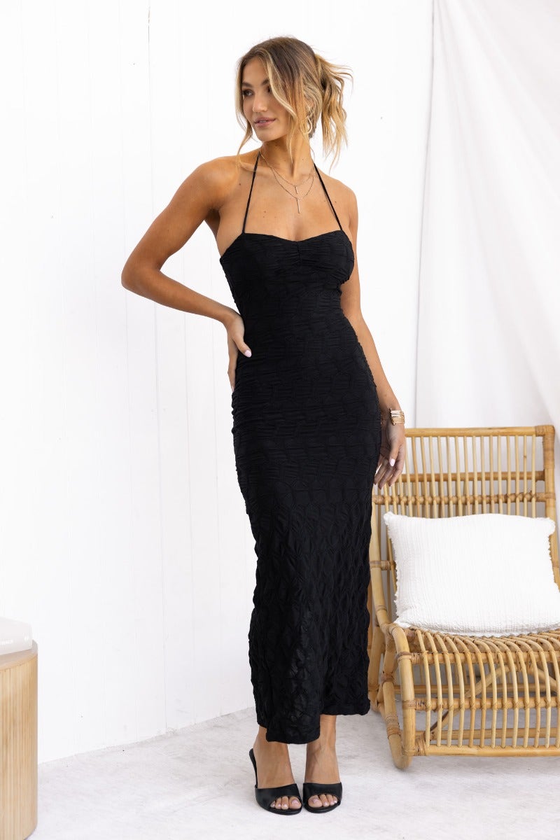 Model in a black textured maxi dress with adjustable halter neckline and split at back, styled with heels.