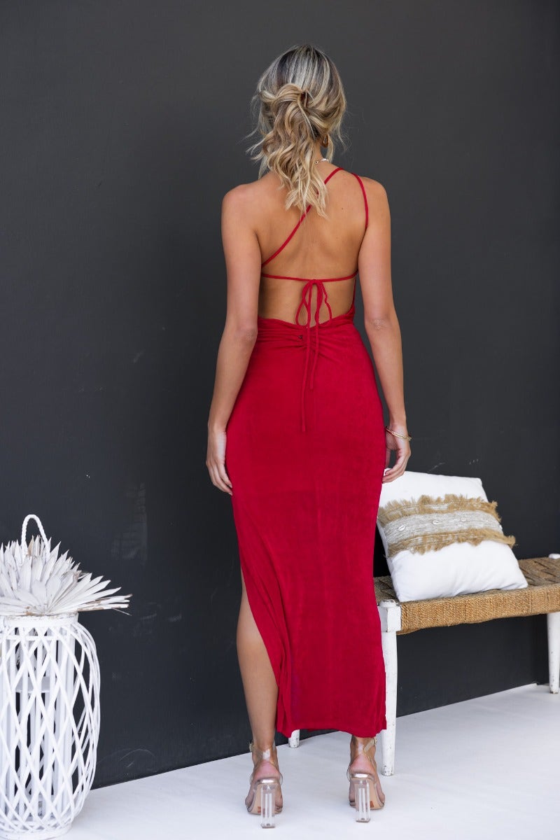 Model wearing a red bodycon maxi dress with a one-shoulder neckline and back tie detail, showcasing a front split.