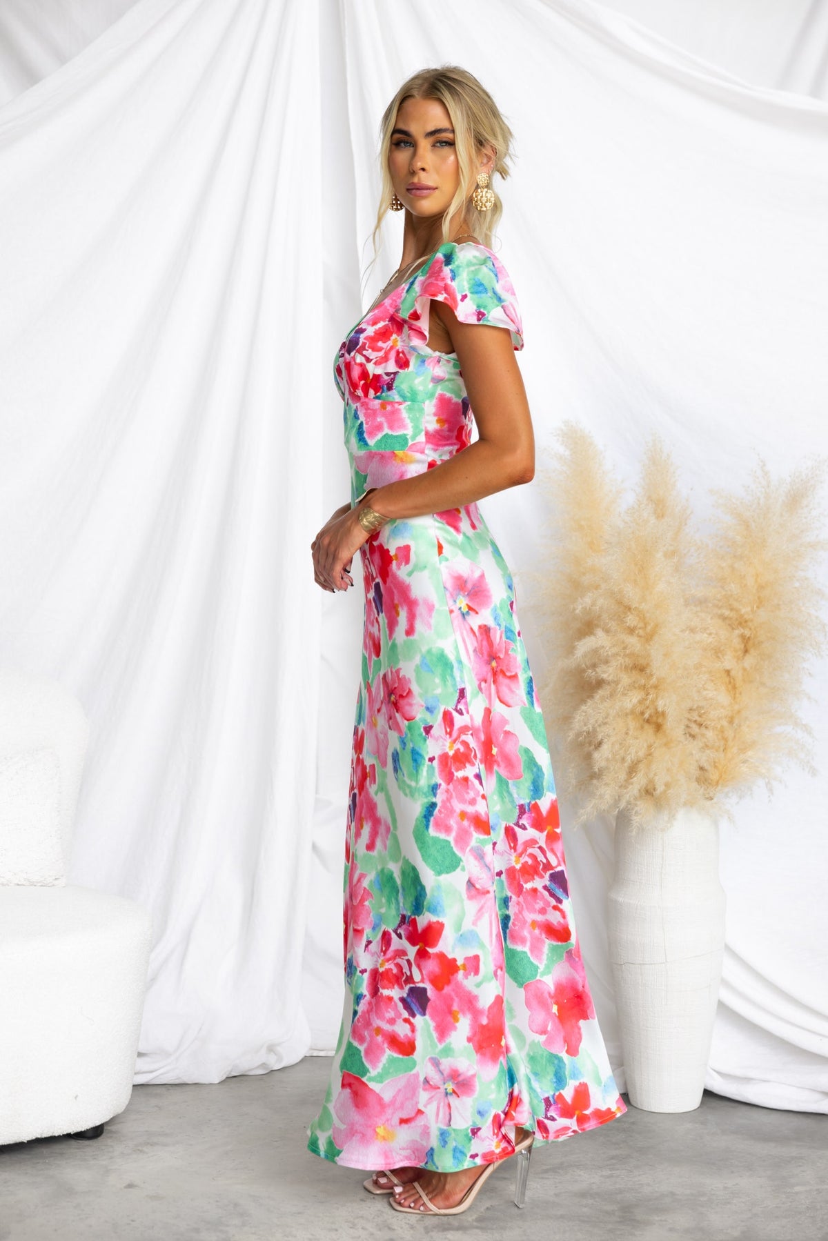 Side view of a woman in a floral satin Belmont maxi dress with cap sleeves against a white backdrop.