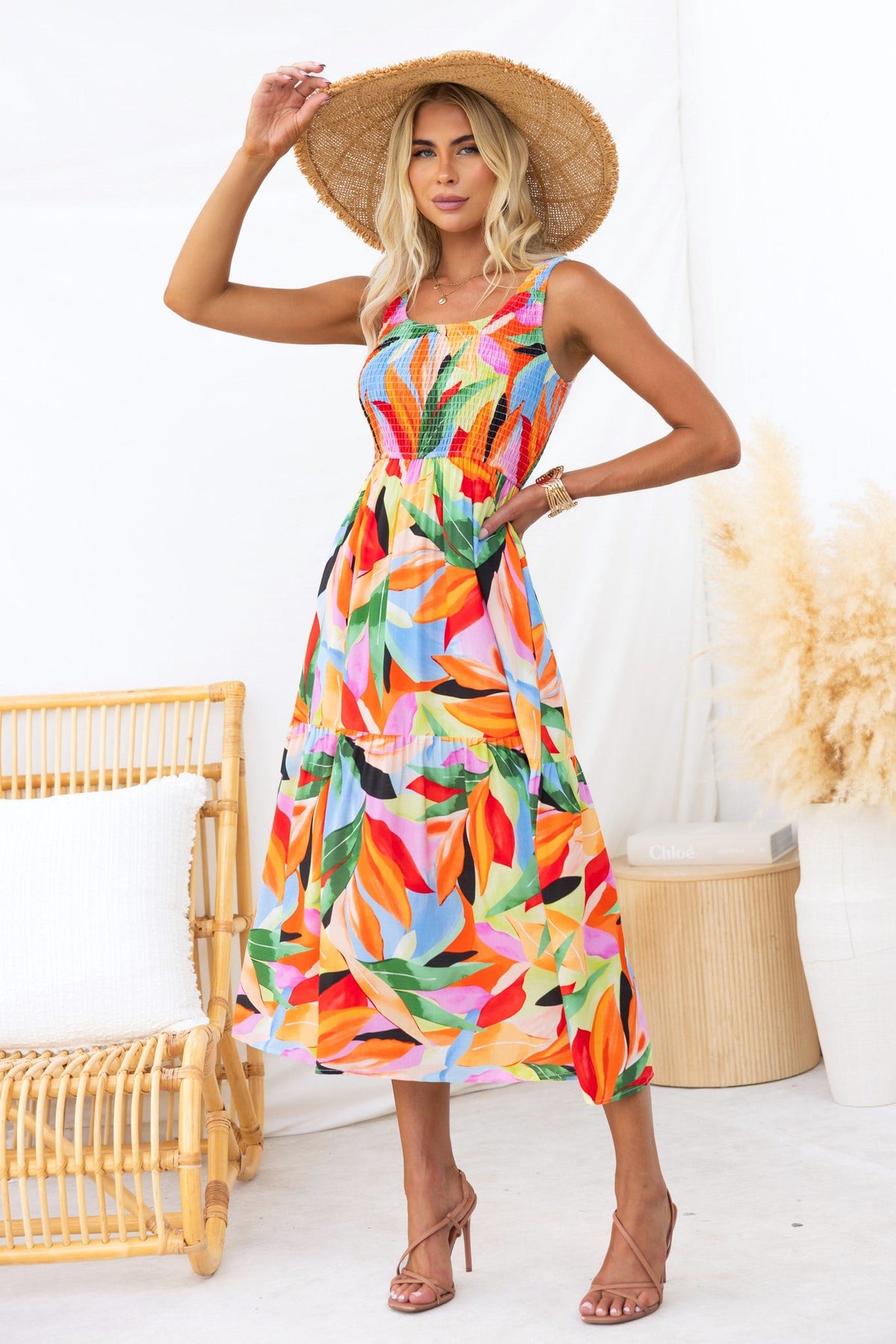 Model wearing Lemi Midi Dress featuring tropical floral print, round neckline, and pockets, styled with a straw hat.