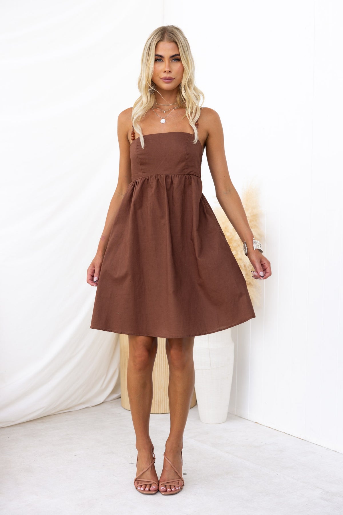 Model wearing the Osment brown mini dress with a square neckline, adjustable straps, and pockets.
