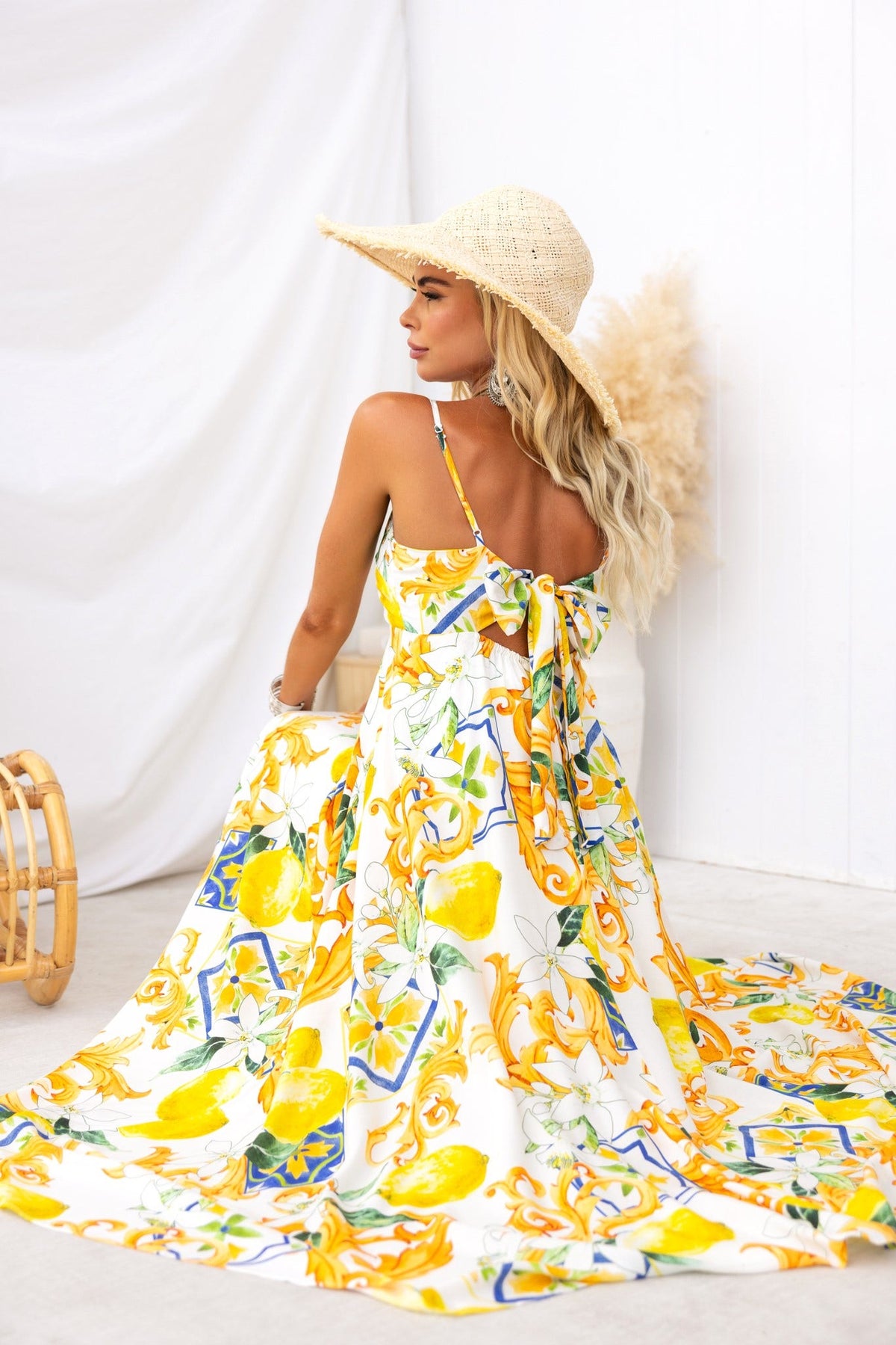 Woman wearing a Summer Crush Maxi Dress with lemon print, adjustable straps, and fabric tie, styled with a straw hat.