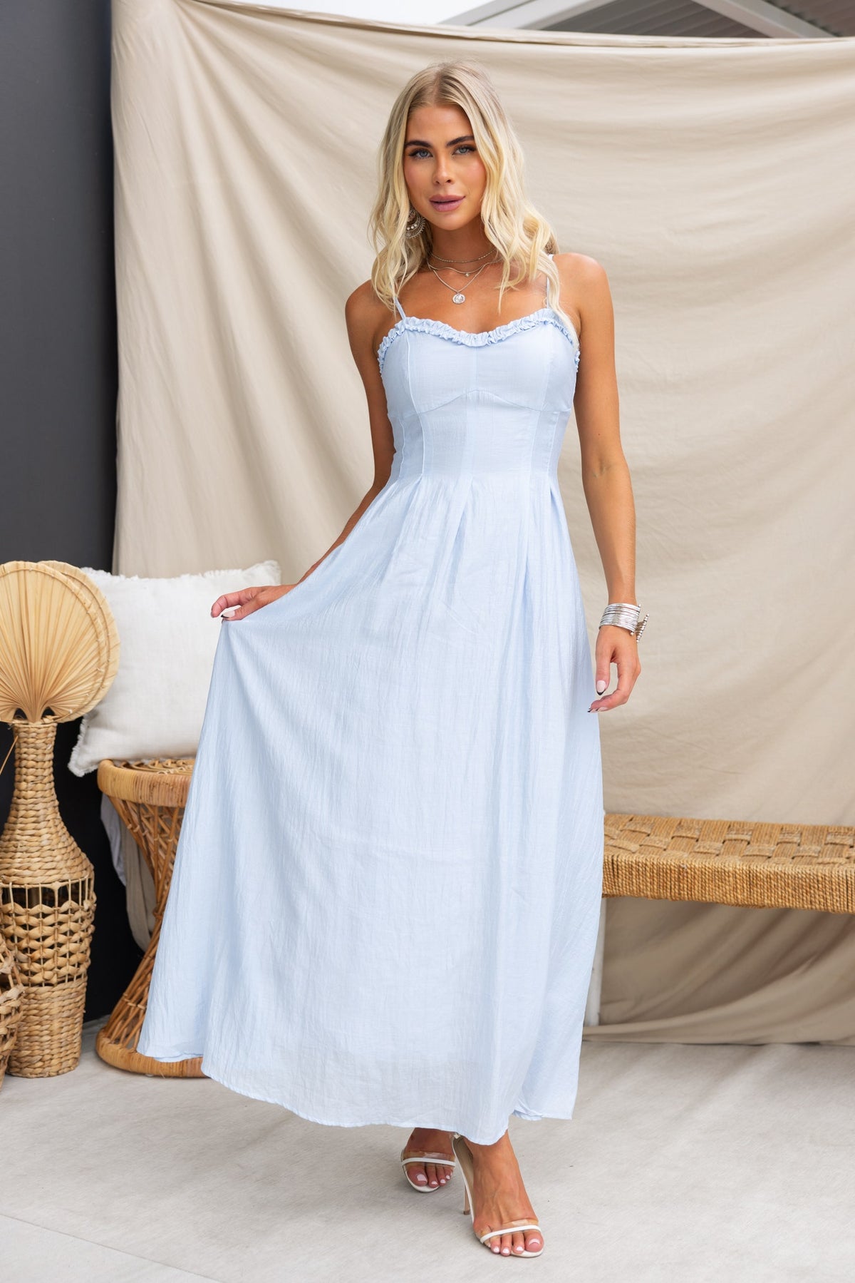 Model wearing Elettra Maxi Dress in light blue, featuring adjustable straps and a flowing design, styled with minimal accessories.