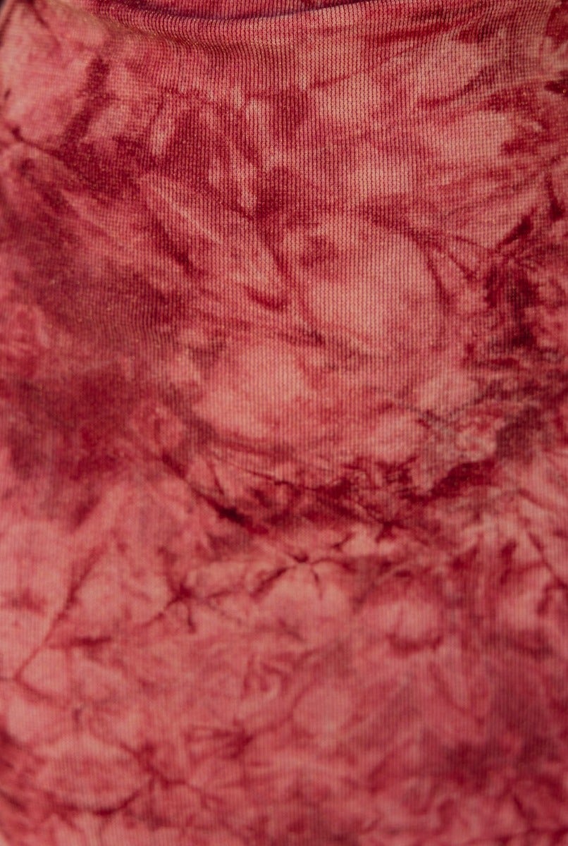 Close-up of a textured, multi-colored fabric featuring shades of red and pink in a tie-dye pattern.