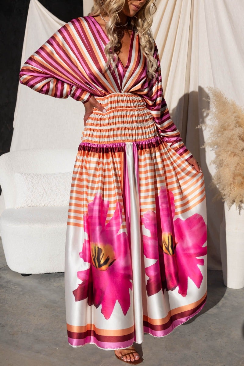 Model wearing Flaria Maxi Dress featuring vibrant floral print, V-neckline, and batwing sleeves with elastic waist.