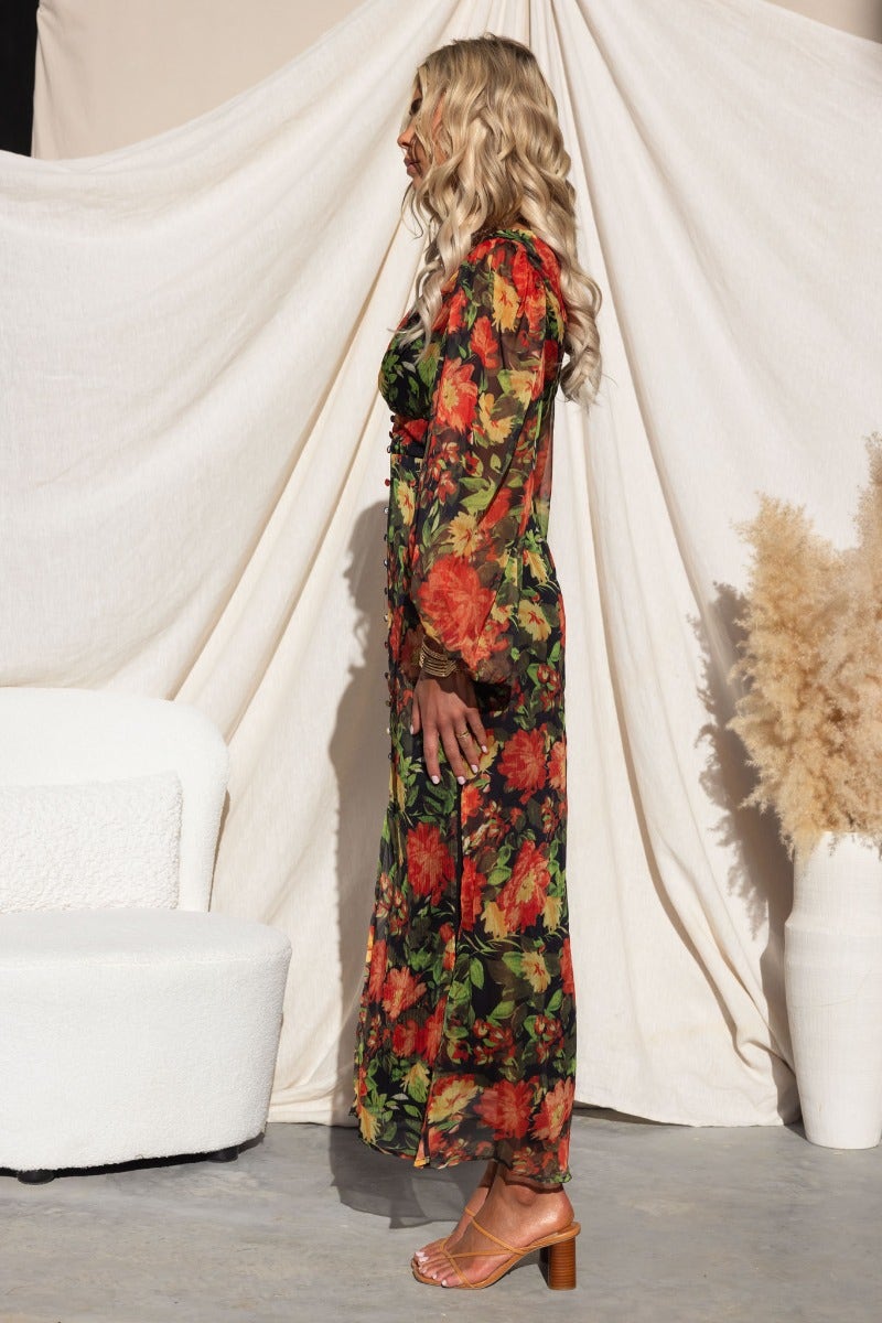 Side view of a model in a floral print Mietta Maxi Dress, featuring a V-neckline and long sleeves, styled with a modern aesthetic.