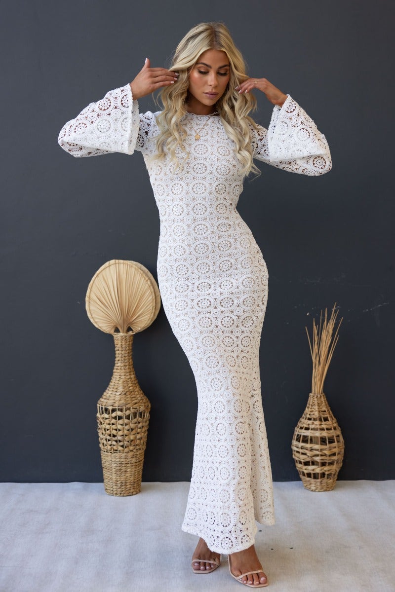 Model showcases Emory Maxi Dress: white crochet with flare sleeves and low back, perfect for summer events.
