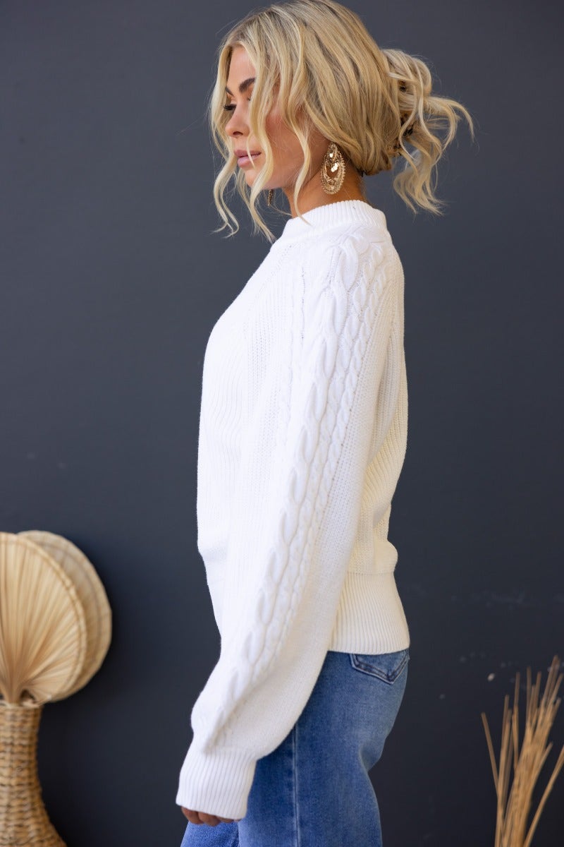Kallan jumper in white, featuring a high neckline, cable knit sleeves, and wide sleeves, model wearing a size 6/XS.