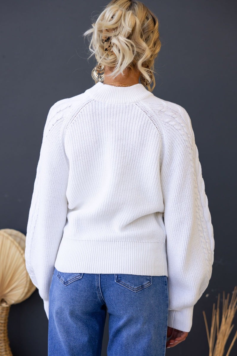 Back view of Kallan Jumper featuring a high neckline, cable knit details, and wide sleeves in white.