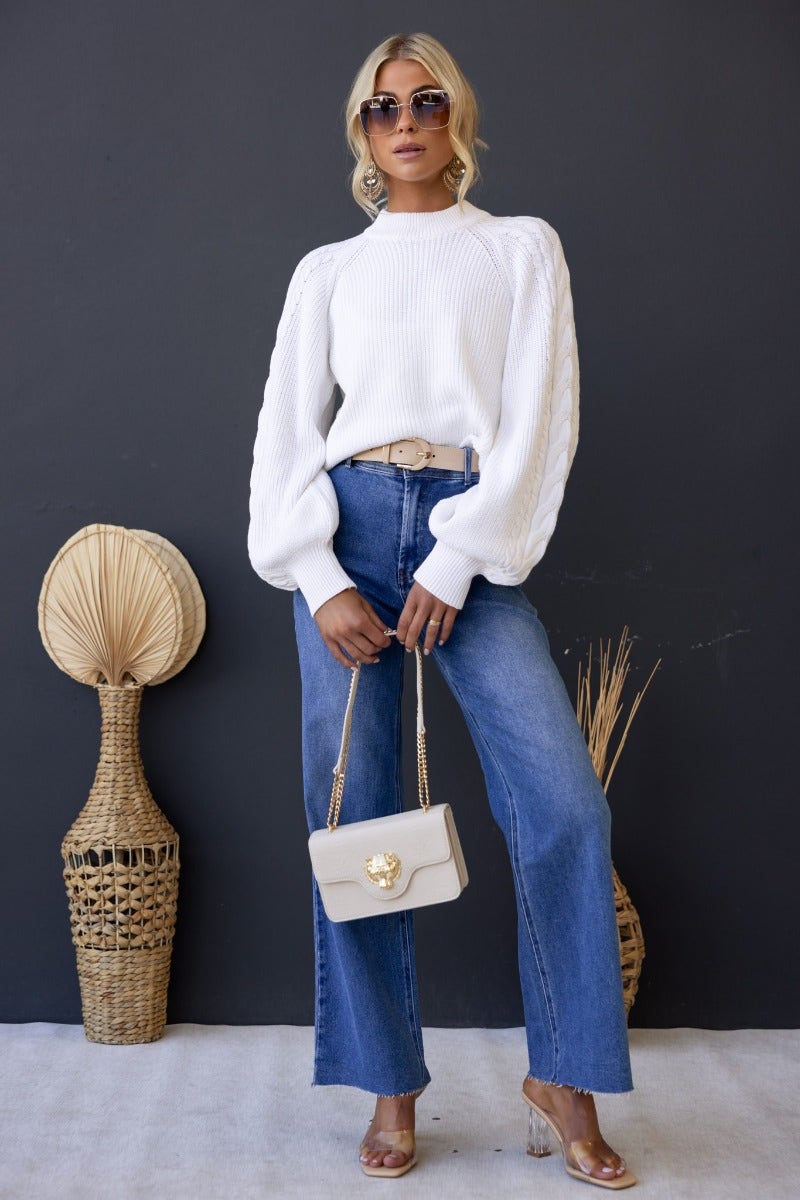 Model wearing Kallan Jumper, a white cable knit sweater with wide sleeves, paired with high-waisted jeans and accessories.