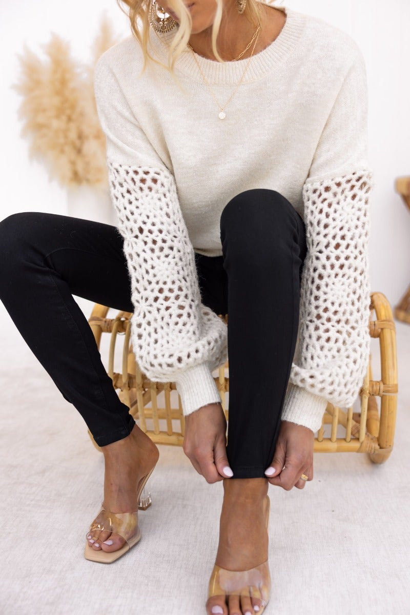 Keilor Jumper featuring open weave knit sleeves, round neckline, paired with black leggings and stylish sandals.