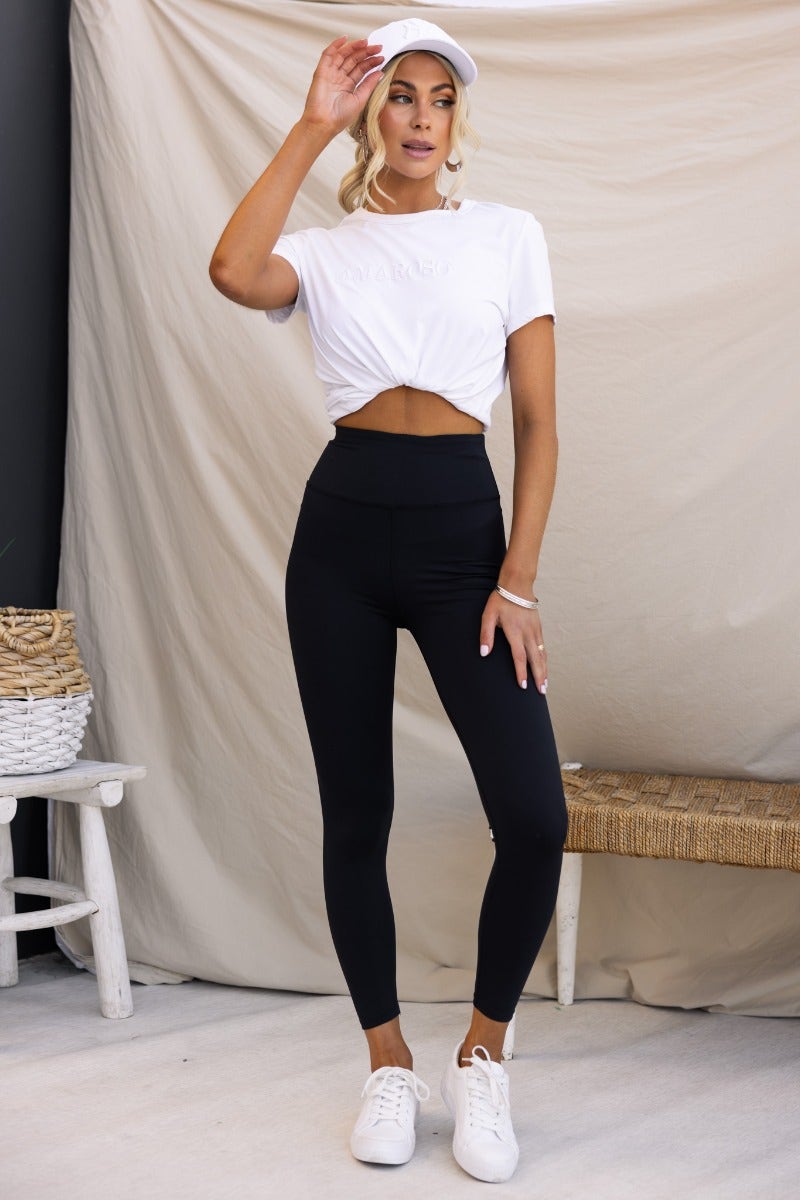 Model wearing black Mally leggings with a mid-high waist and wide waistband, styled with a white crop top and sneakers.