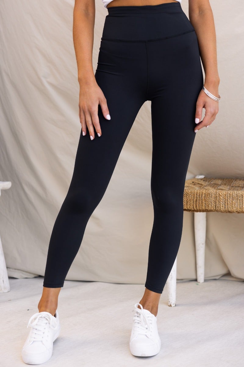 Mally black leggings with mid-high waist and wide waistband, featuring firm stretch material, worn with white sneakers.