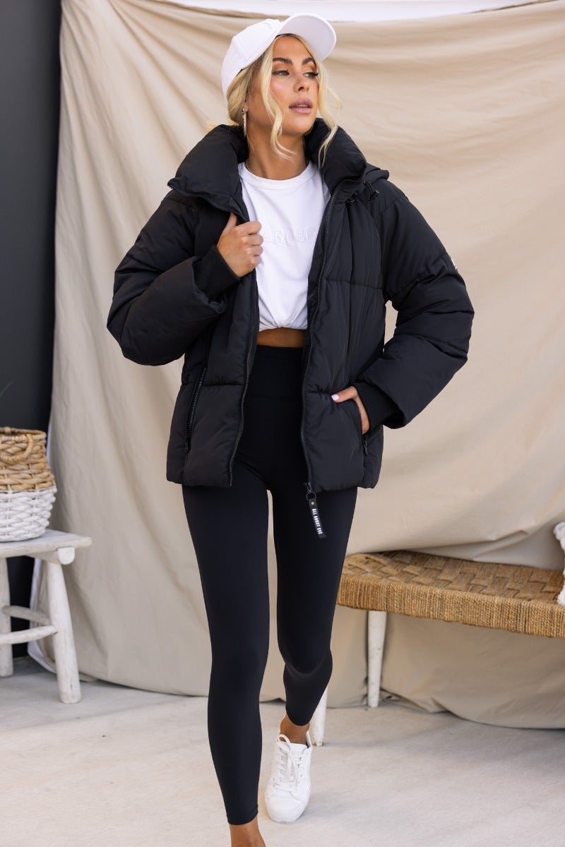 Model wearing Delila black puffer jacket with high neckline, removable hood, and zip-up front.