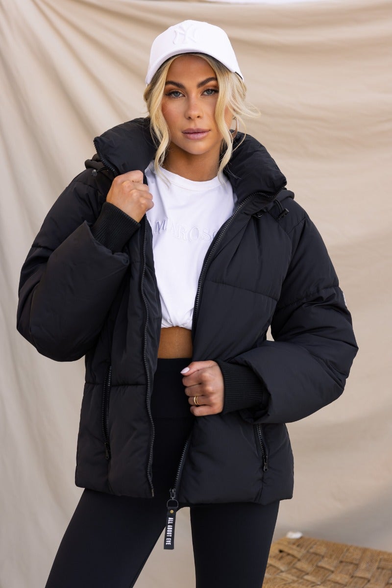 Model wearing a black Delila puffer jacket with a high neckline, removable hood, and zip-up front.