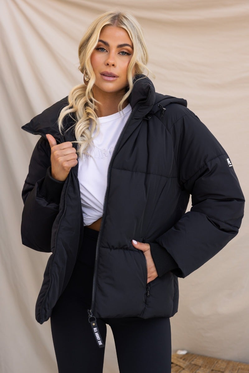 Model wearing a black Delila puffer jacket with a removable hood and zip-up front, showcasing its stylish design.