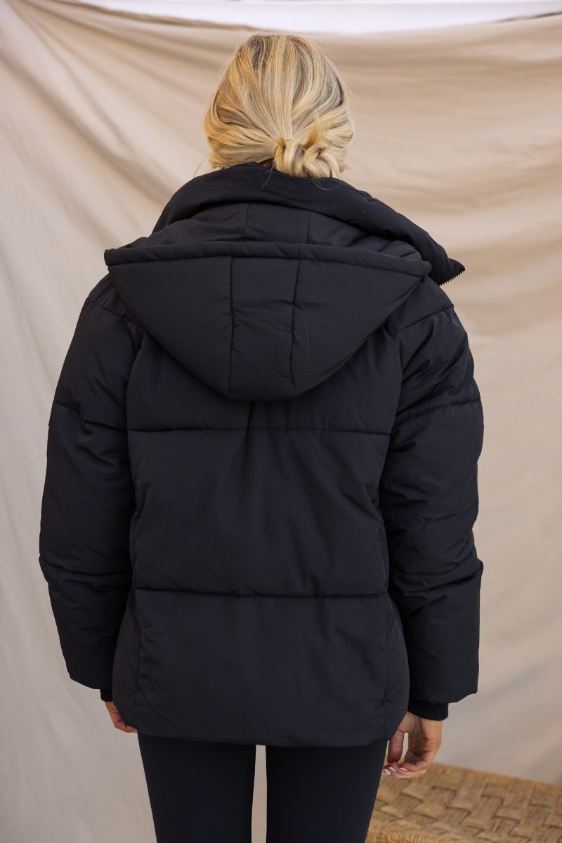 Back view of the Delila Black Puffer Jacket featuring a removable hood and a high neckline.