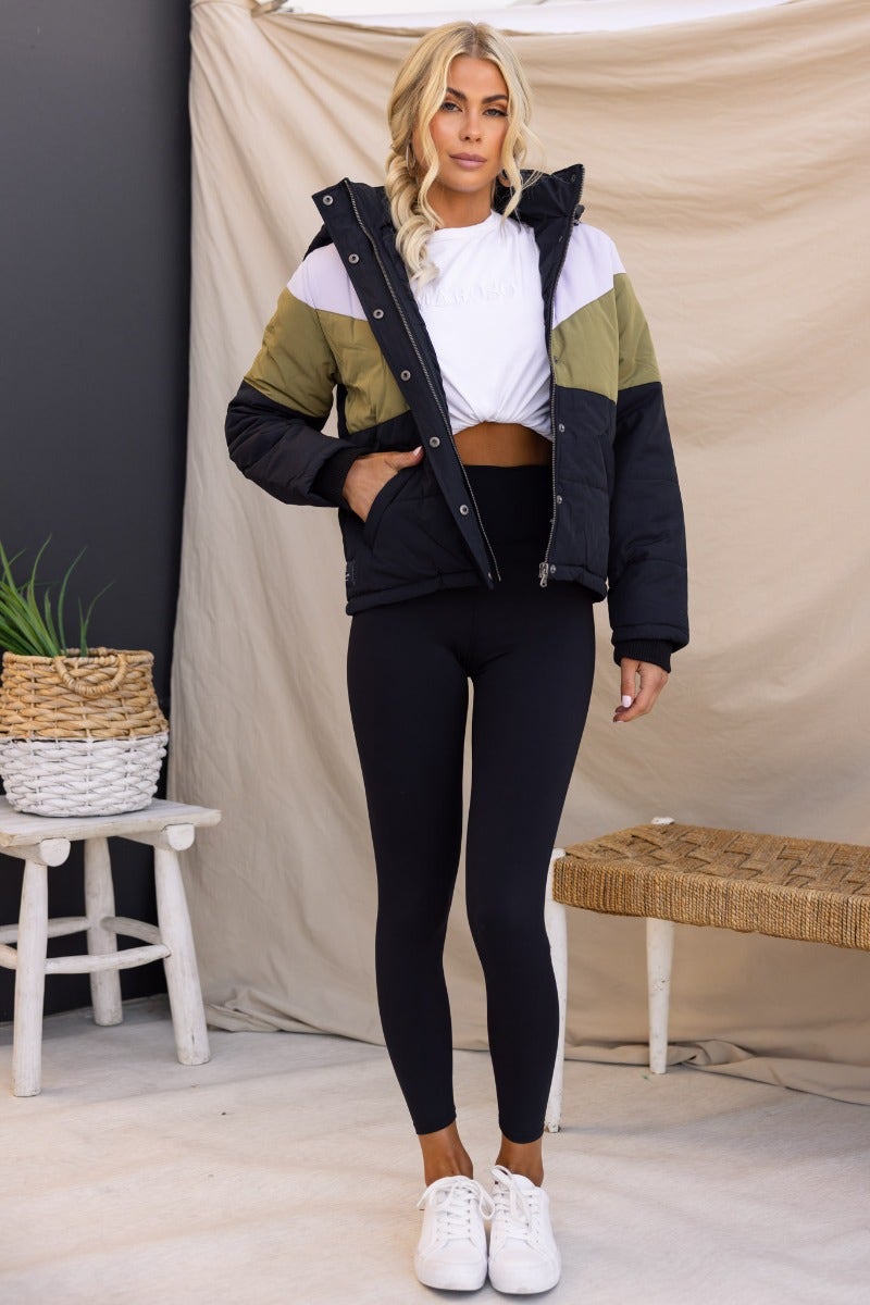 Charis Puffer Jacket featuring a black, olive, and white design, worn by a model with leggings and sneakers.