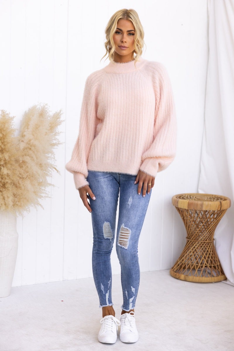 Model wearing a fluffy pink jumper with wide sleeves, paired with ripped jeans and white sneakers.