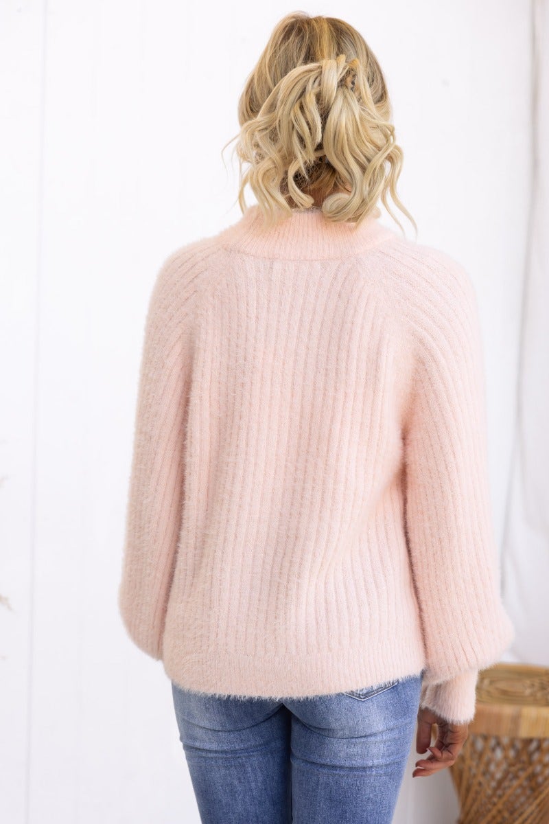 Back view of a fluffy pink knit Jaylin Jumper featuring wide sleeves and a high neckline, styled with jeans.