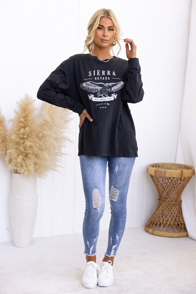 Model wearing oversized Sierra Nevada print long sleeve top with distressed jeans and white sneakers.