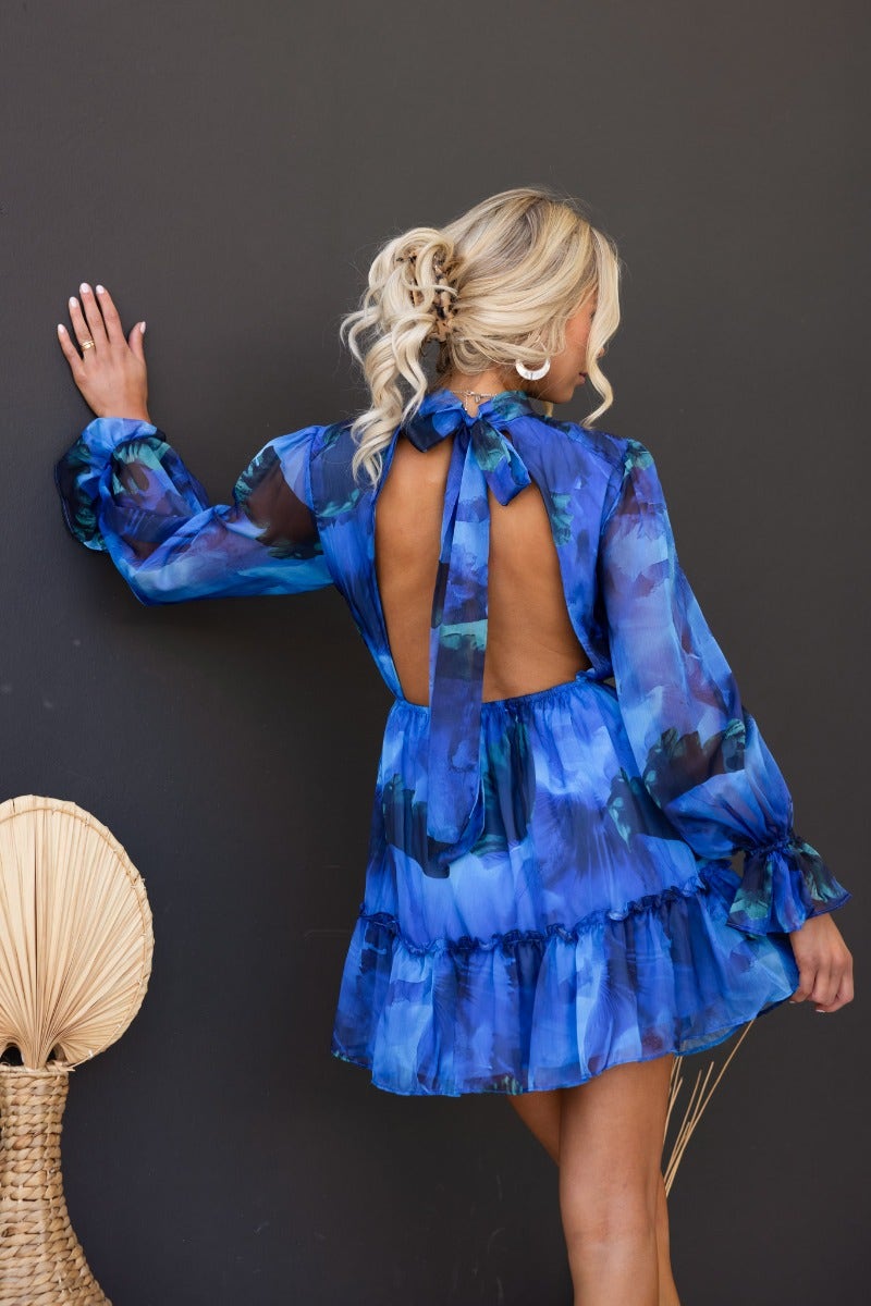Model wearing Our Chance Dress in blue floral print with open back and tie detail, styled with a chic hairstyle.