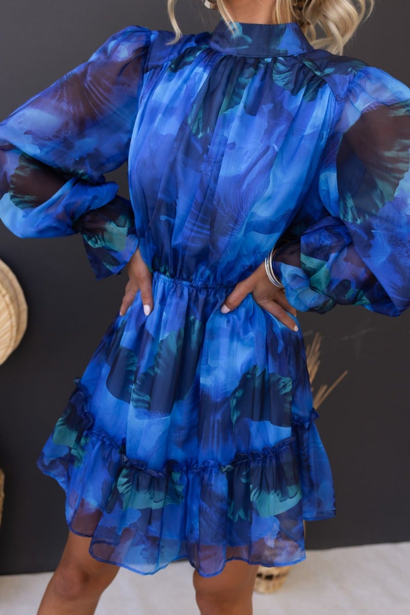 Model in a multi-color dress featuring a high neckline, tie detail, and open back with elastic waist and cuffs.