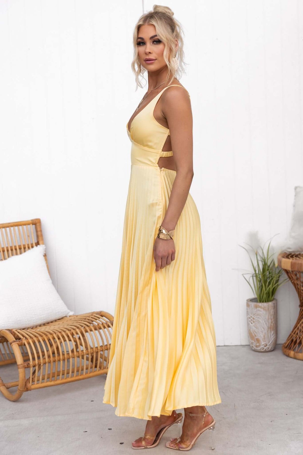 Side view of a woman wearing a yellow Janisse Maxi Dress with a pleated skirt and adjustable straps.