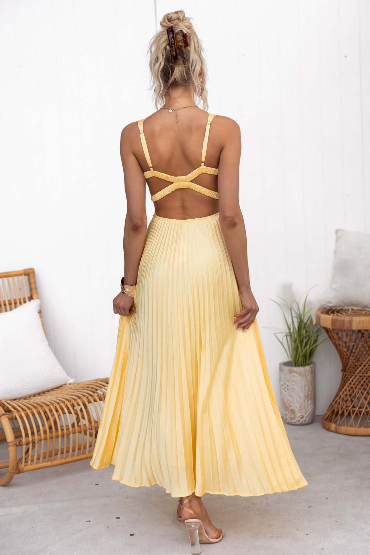 Back view of a model wearing a pleated yellow Janisse Maxi Dress with adjustable straps.