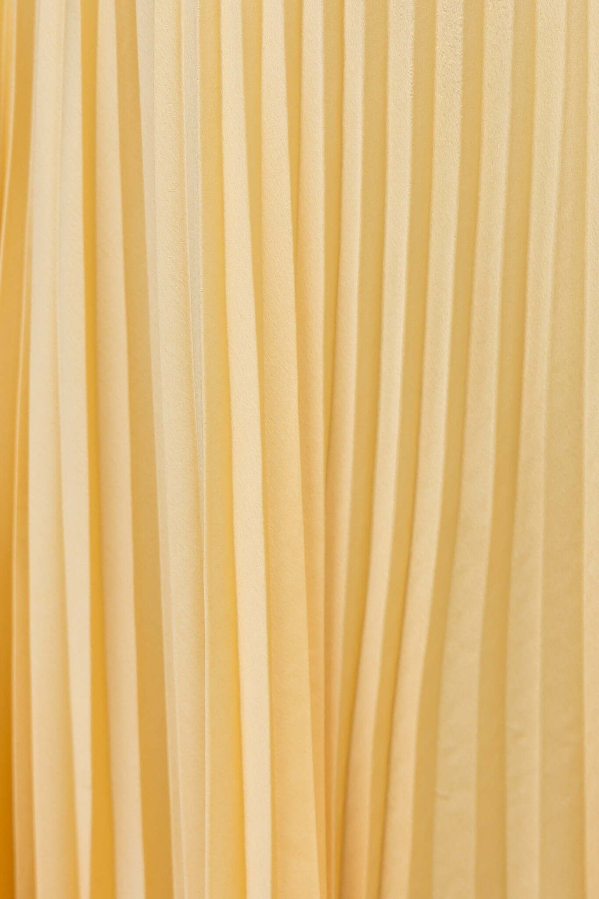 Close-up of pleated yellow fabric showcasing the elegant texture of the Janisse Maxi Dress.