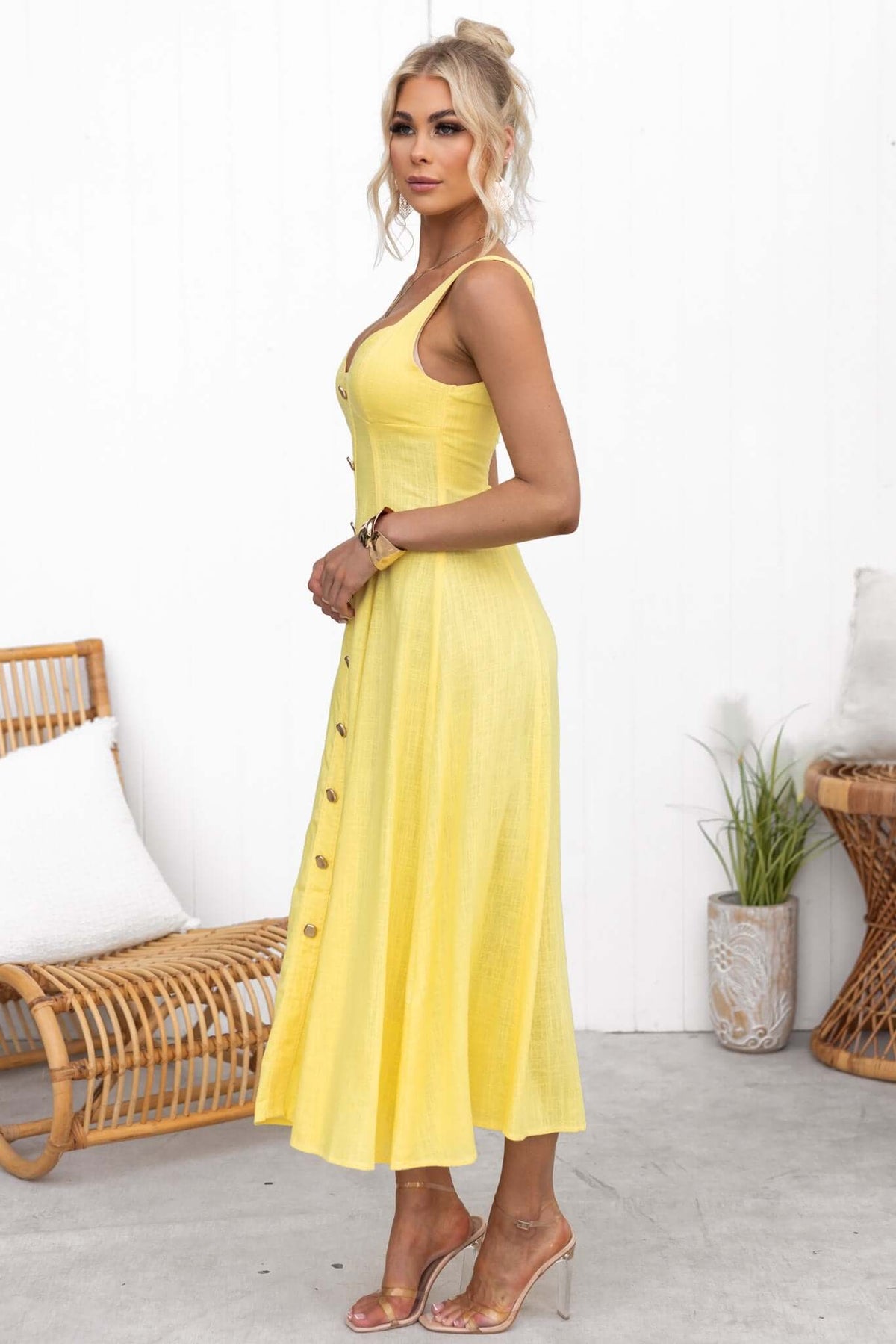 Side view of a woman wearing a yellow Lyre Midi Dress with faux buttons and a flowing skirt.