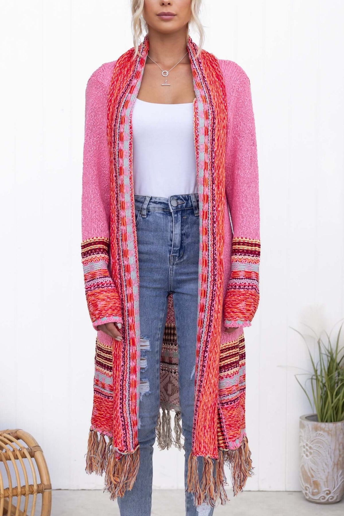 Model wearing a pink longline Lewis Cardigan with tassels, styled with a white top and jeans.