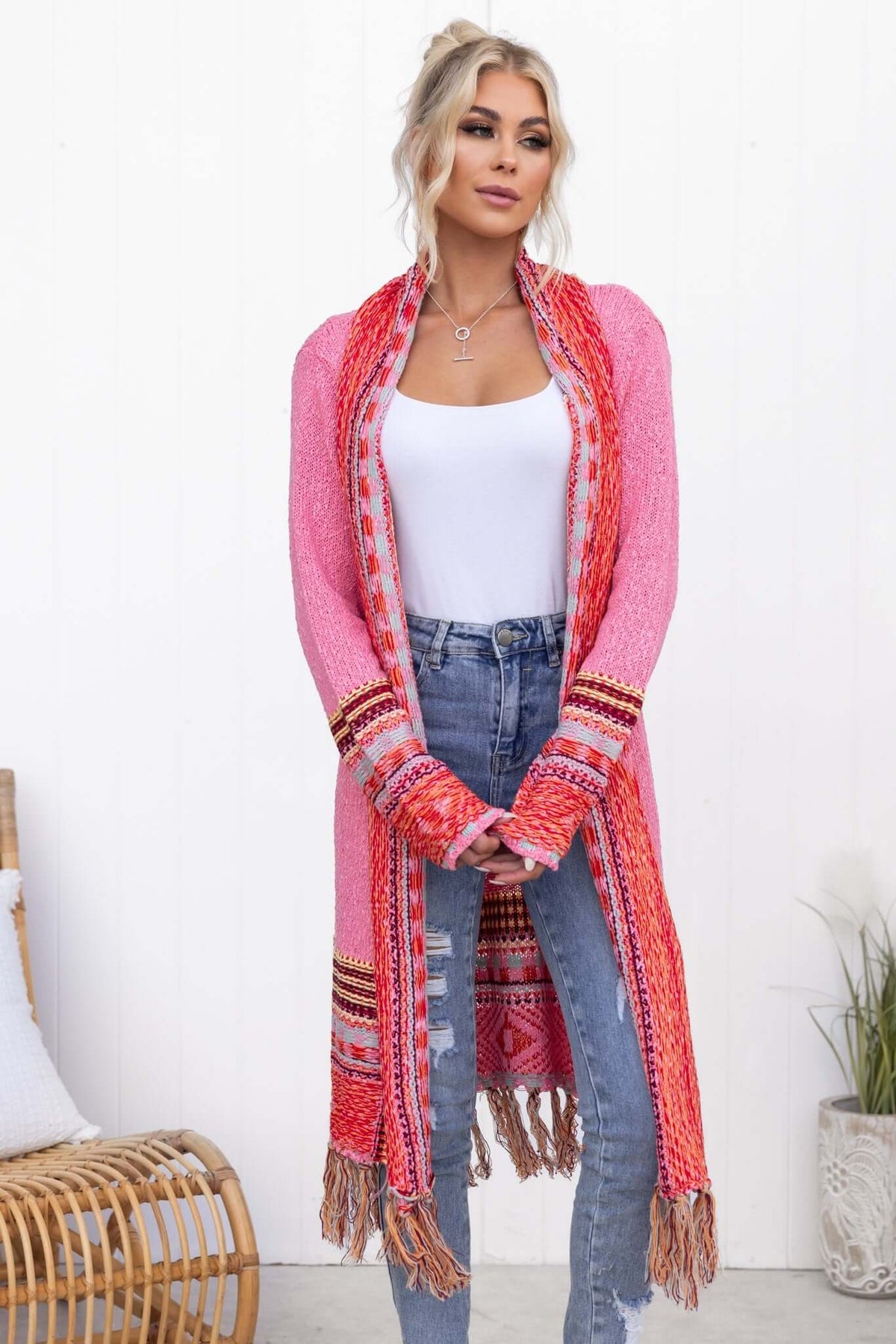 Lewis Cardigan in pink and red, featuring a longline fit and tassels, styled with jeans and a white top.