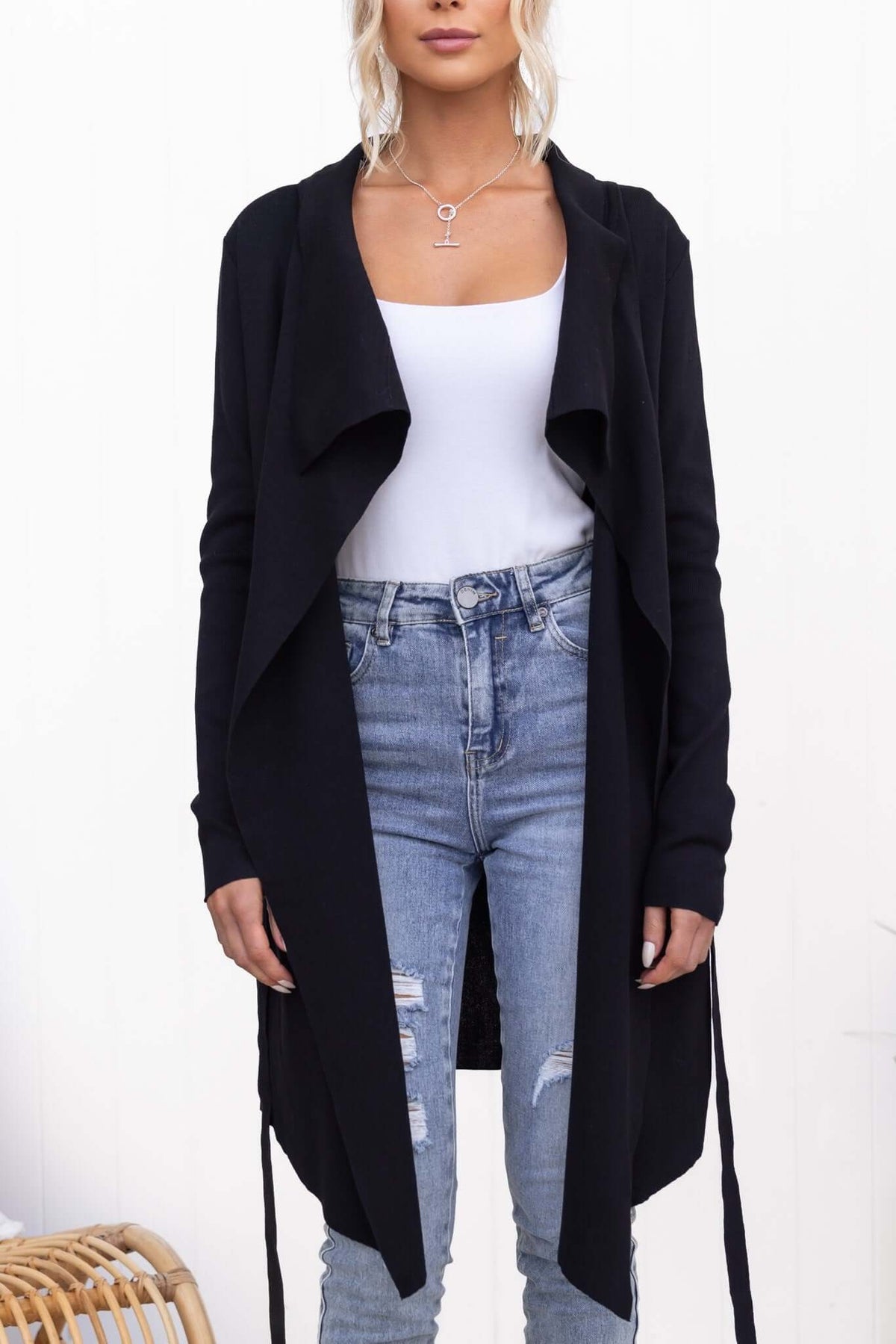 Model wearing Acaia Cardigan in black ribbed knit with pockets and attached belt, paired with ripped jeans.