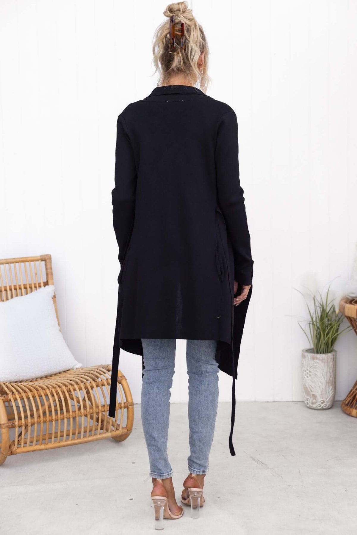 Back view of a woman in a black Acaia cardigan with pockets, paired with blue jeans and stylish heels.
