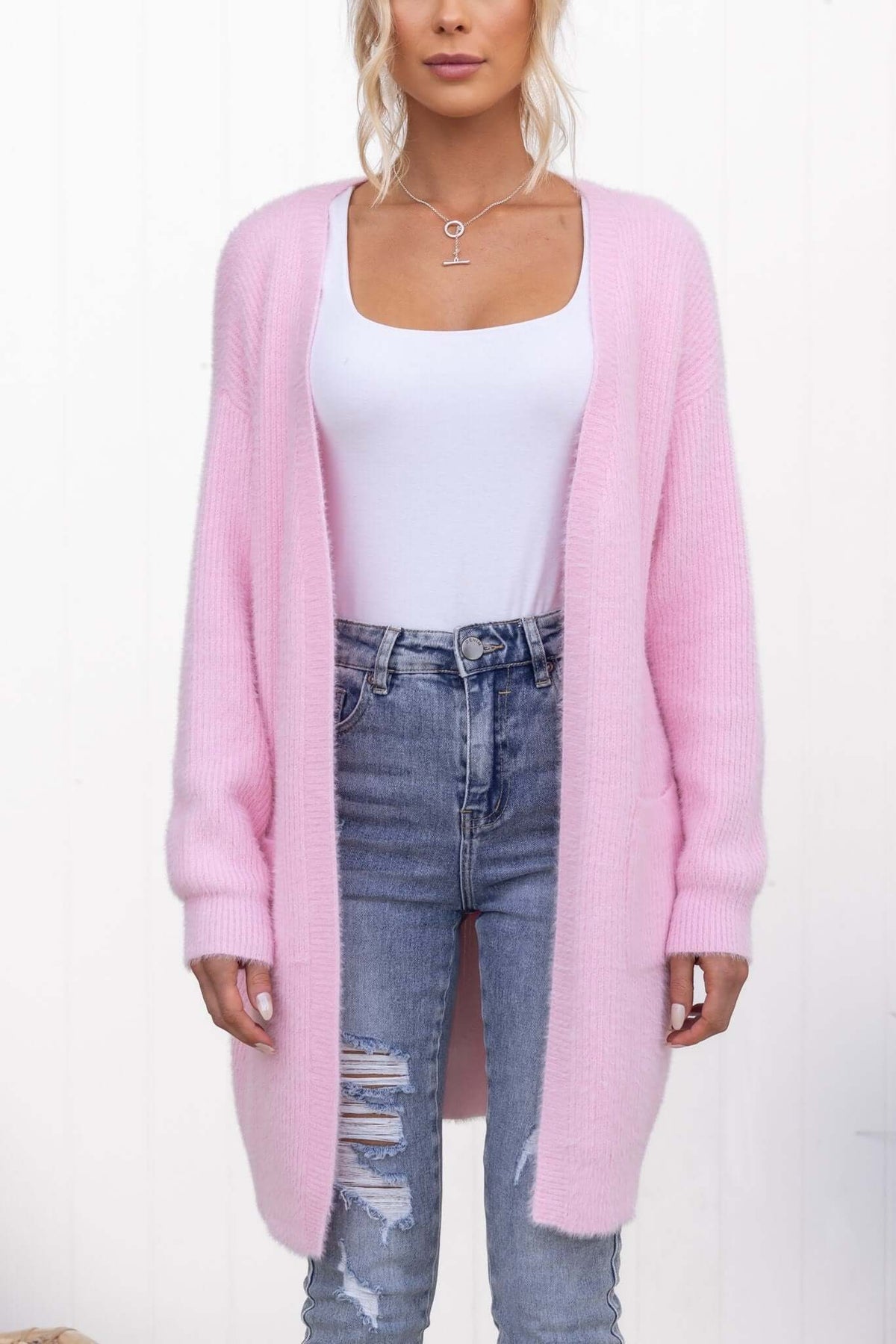 Fluffy longline pink cardigan with pockets, styled over a white top and distressed jeans, perfect for casual outfits.