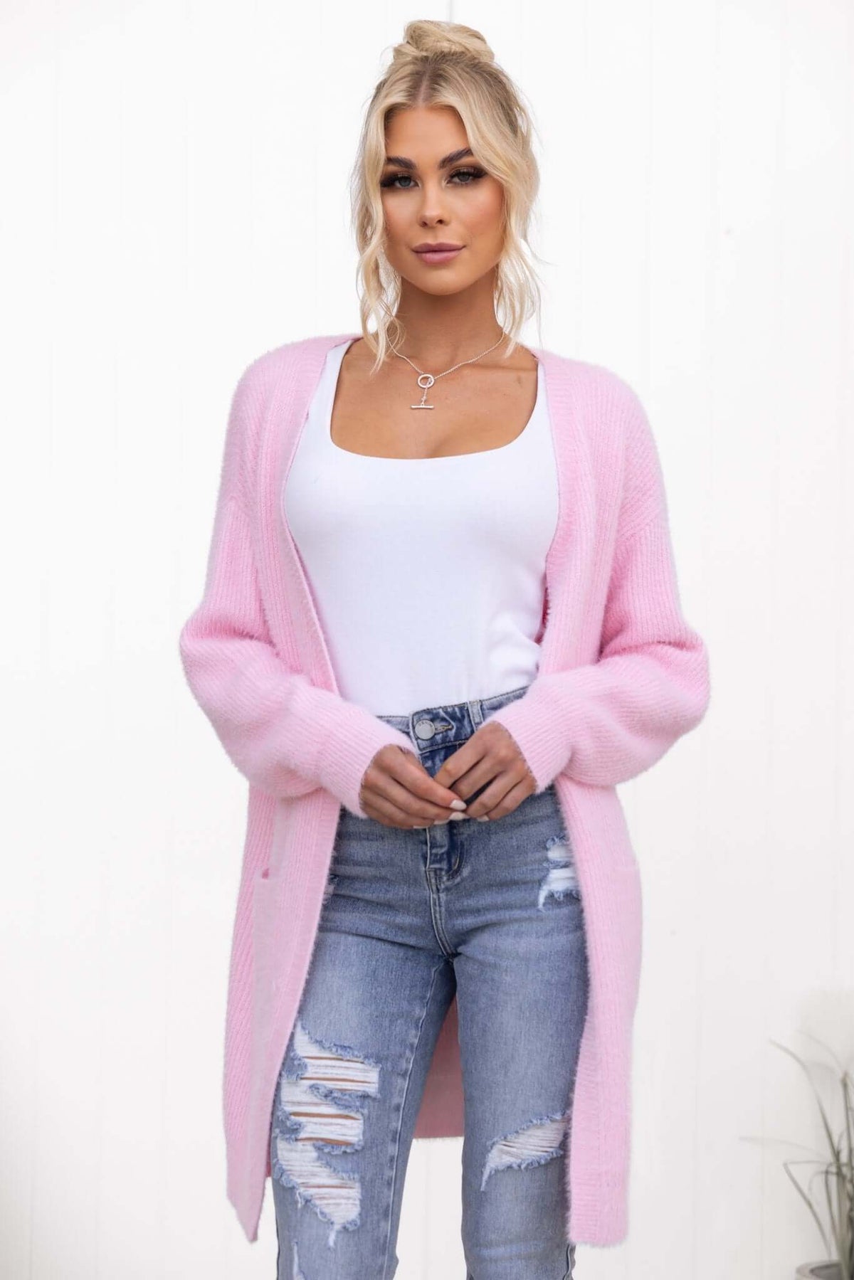 Model wearing a pink Shai Cardigan over a white tank top, styled with distressed jeans in a relaxed fit.