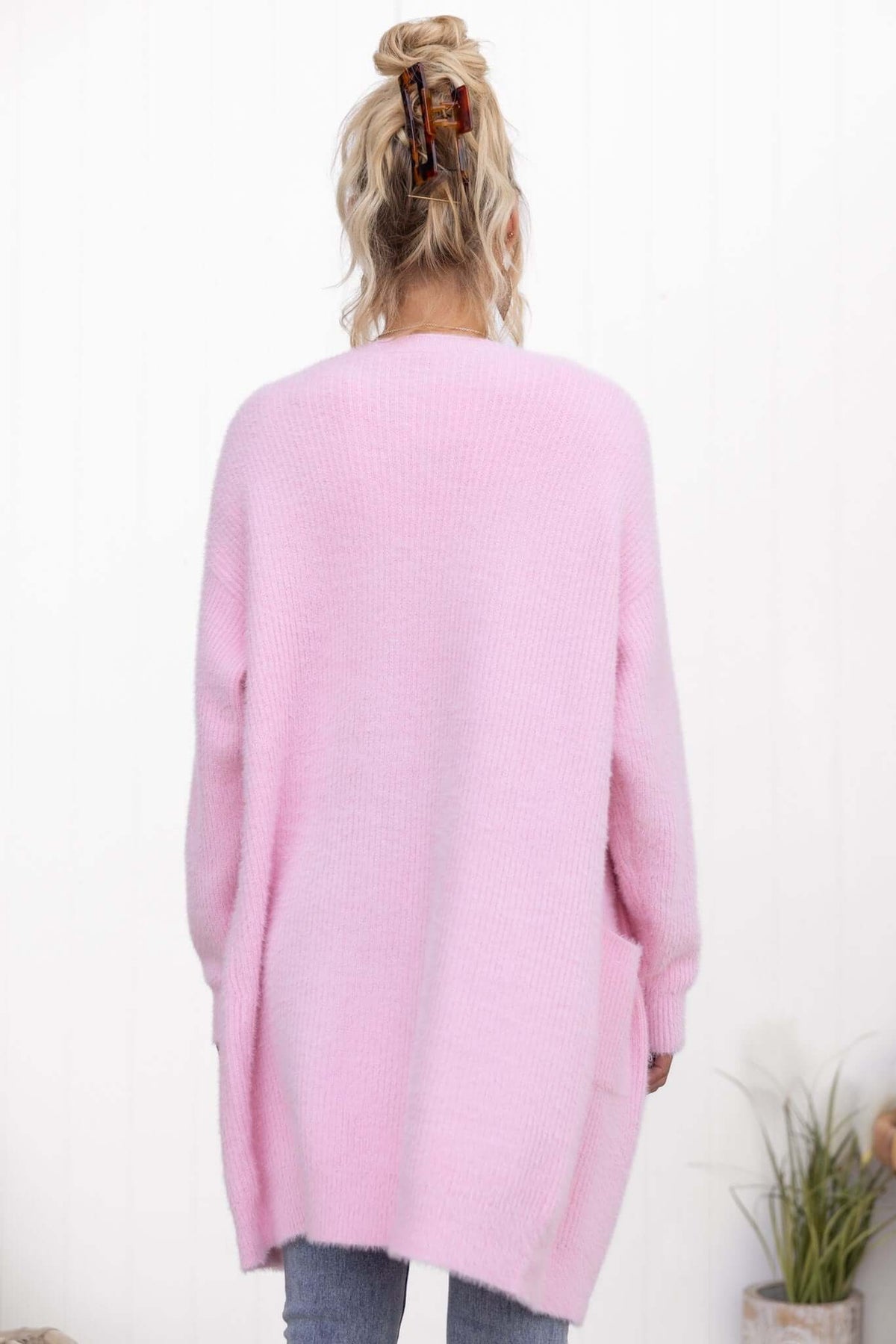 Back view of a relaxed fit pink Shai Cardigan with pockets, made of fluffy knit material, styled with jeans.