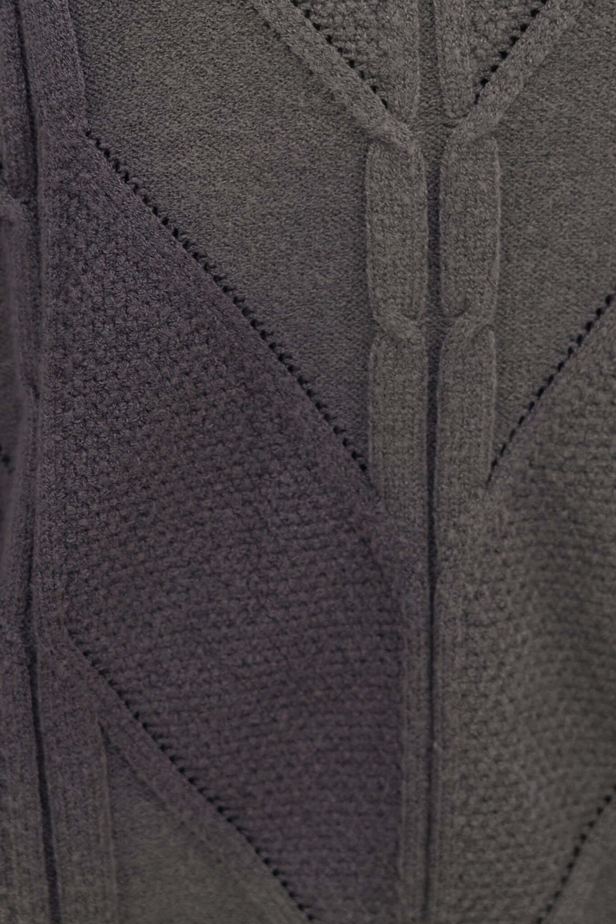 Close-up of a textured grey cable knit fabric showcasing intricate patterns and stitches, ideal for a stylish jumper.
