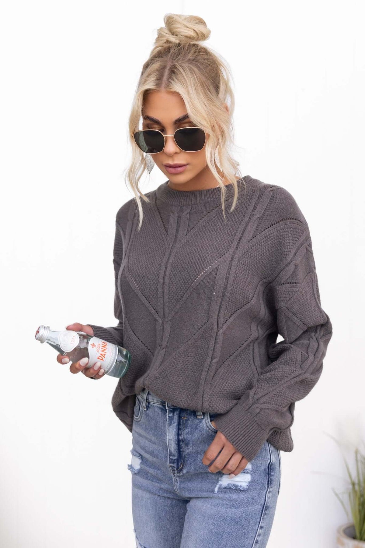 Model wearing Becker Jumper with round neckline and cable knit design, holding a drink, showcasing relaxed fit and style.
